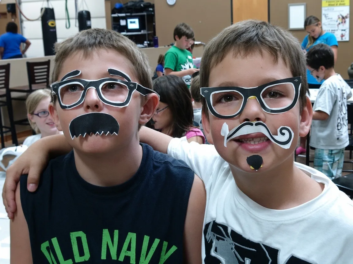Two school-age boys wearing silly glasses and mustache props