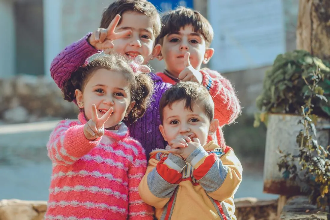 Four young children smiling and making peace signs outdoors