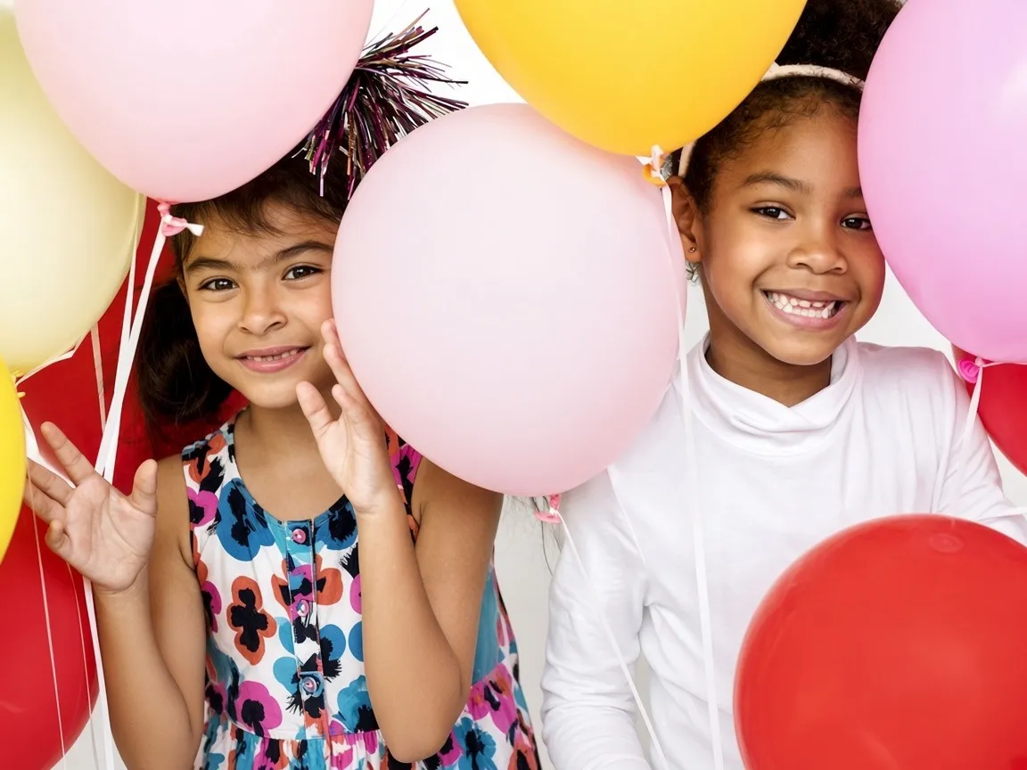 Two girls smiling among pink and yellow birthday balloons
