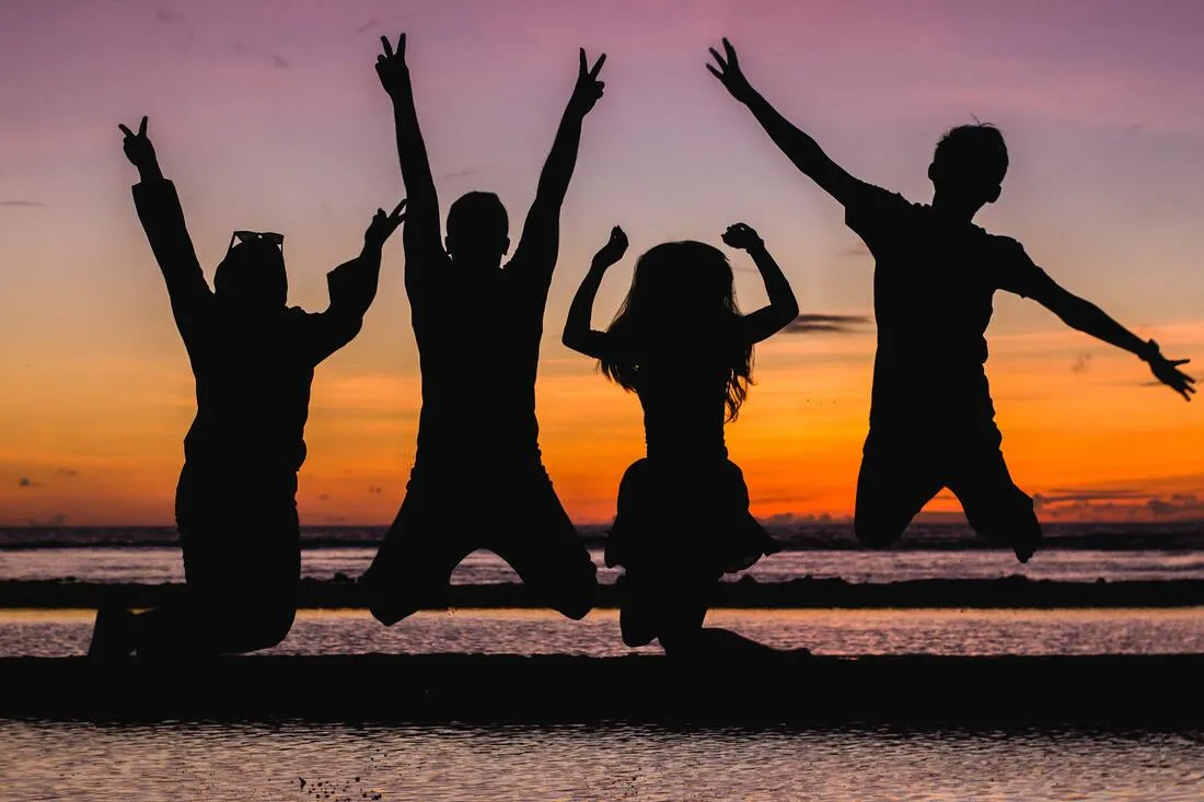 Silhouettes of four children jumping against a sunset