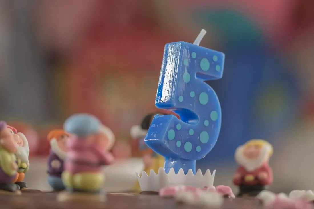 A blue number five birthday candle on a cake