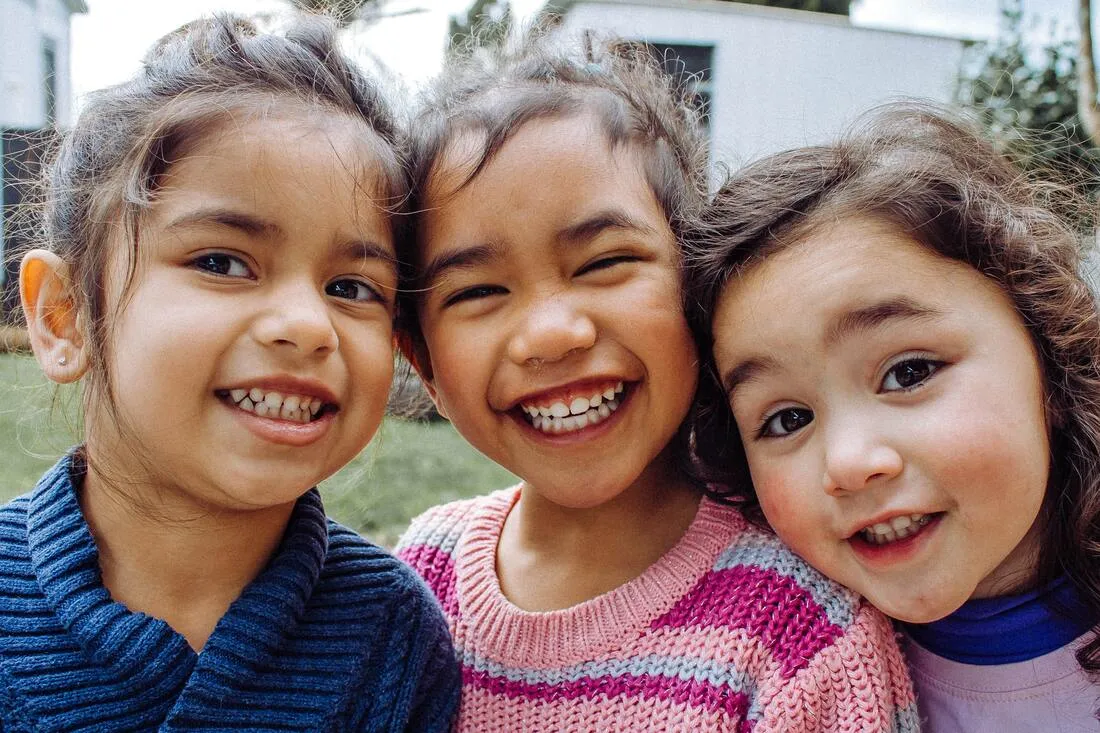 Three smiling young girls posing close together outdoors