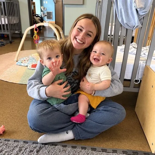 A teacher cuddling with two babies in the infant room