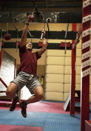 A student swinging across hanging nunchuk holds on the ninja course