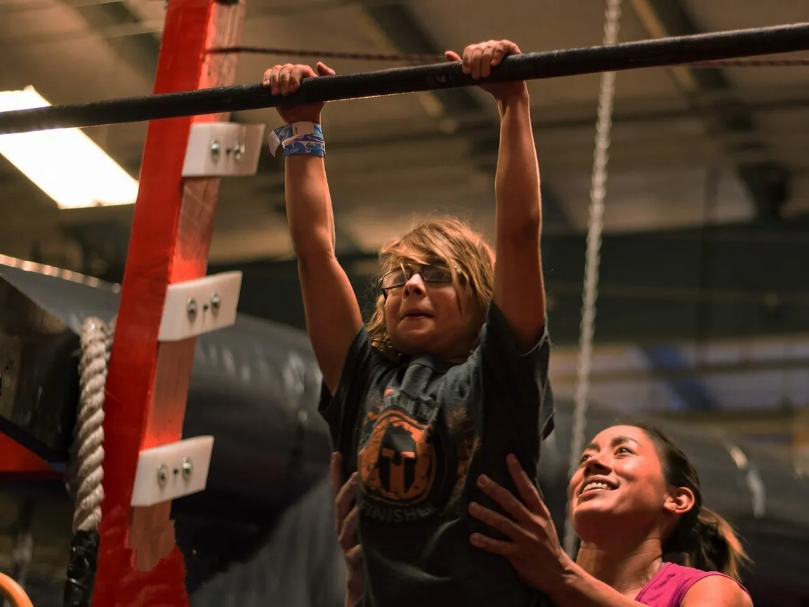 A Bodies in Motion coach spotting a child hanging from a ninja bar