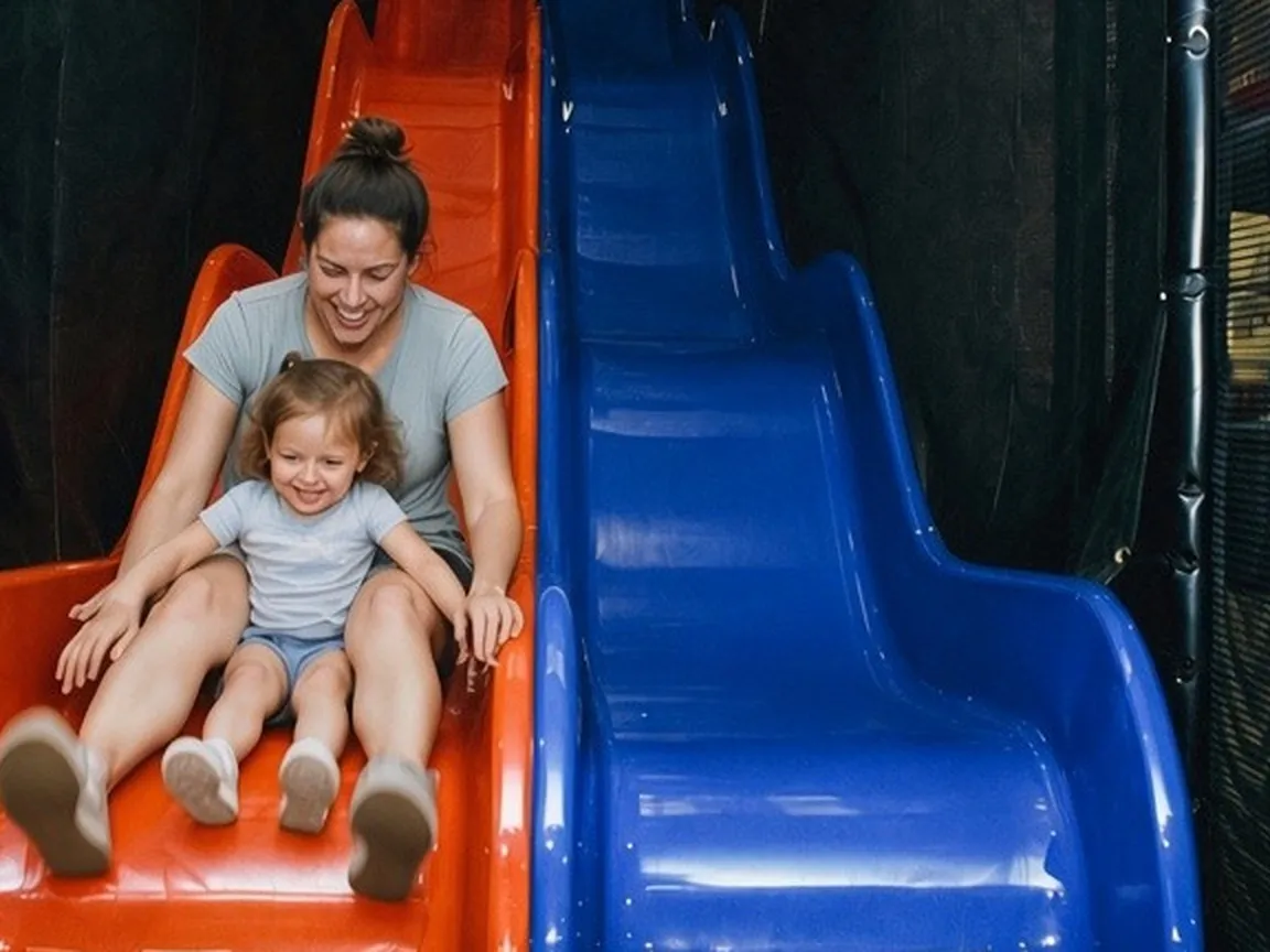 Mom on the left indoor slide with her toddler daughter between her legs