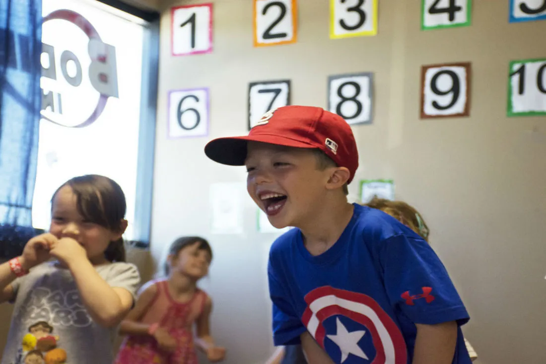A laughing child in a red cap with other children in front of a wall of number cards