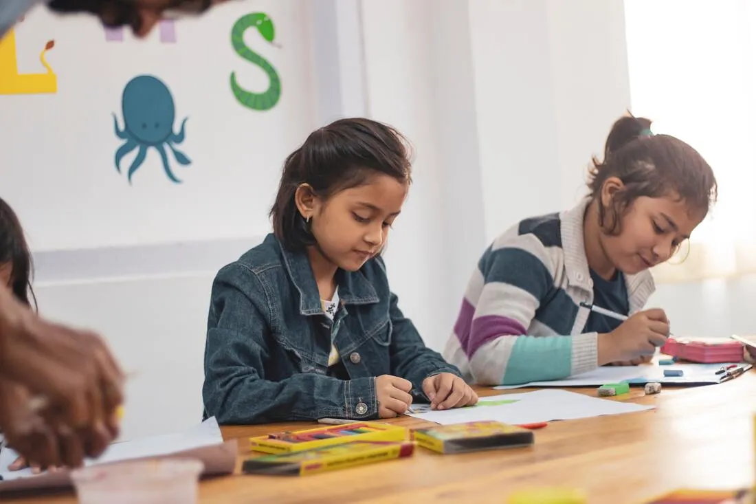 Two girls drawing at a classroom table