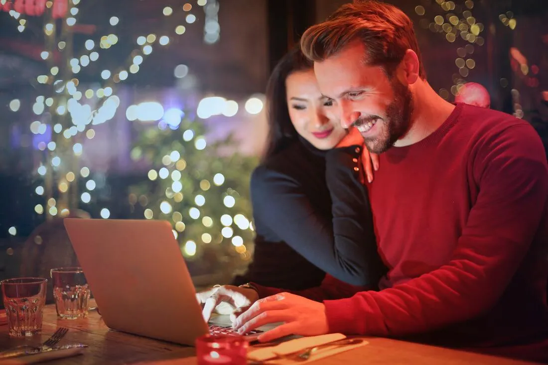 A couple smiling at a laptop in a softly lit restaurant
