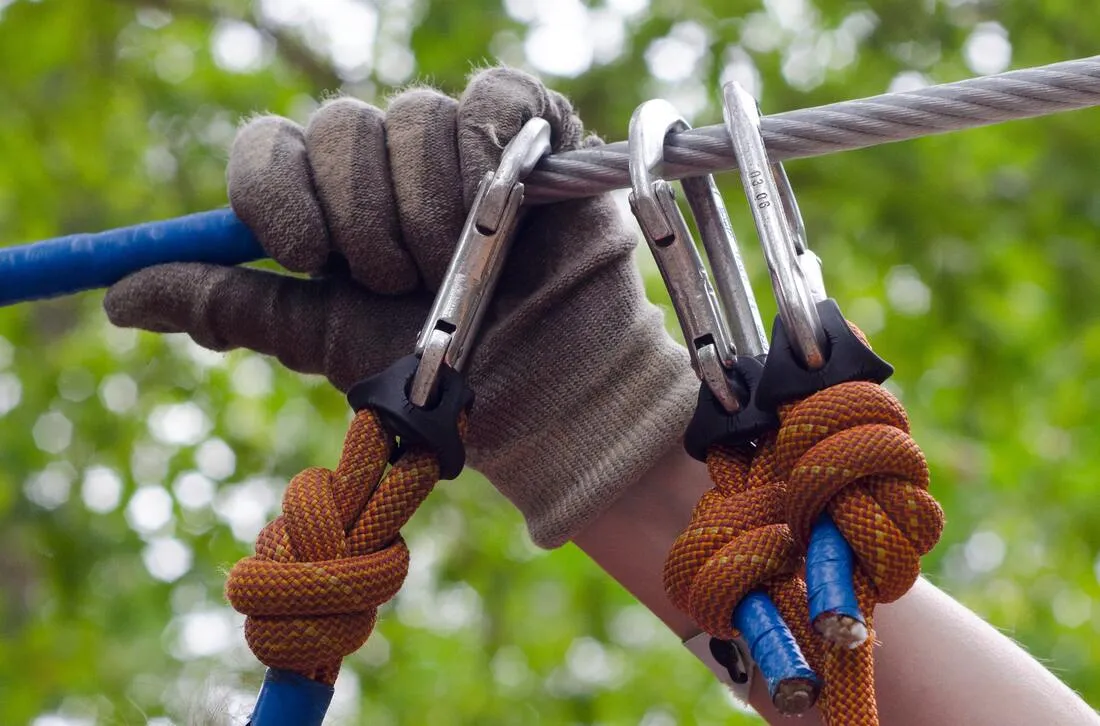 A gloved hand clipped to a cable with carabiners and rope