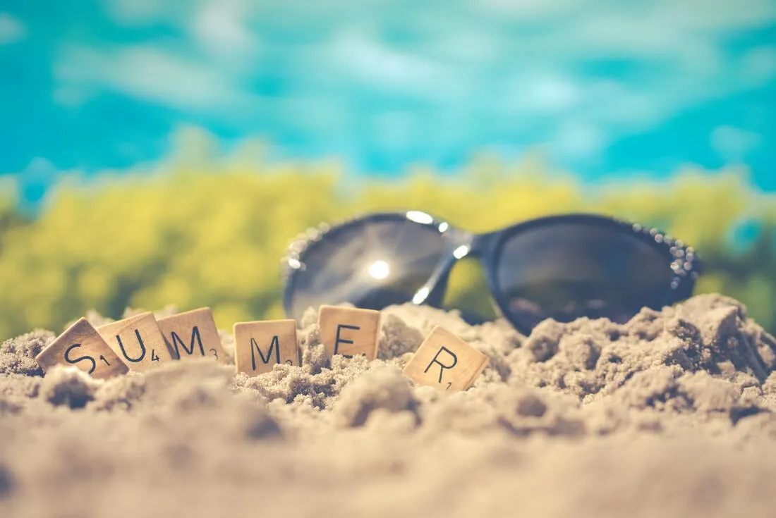 The word SUMMER spelled in tiles in the sand next to sunglasses