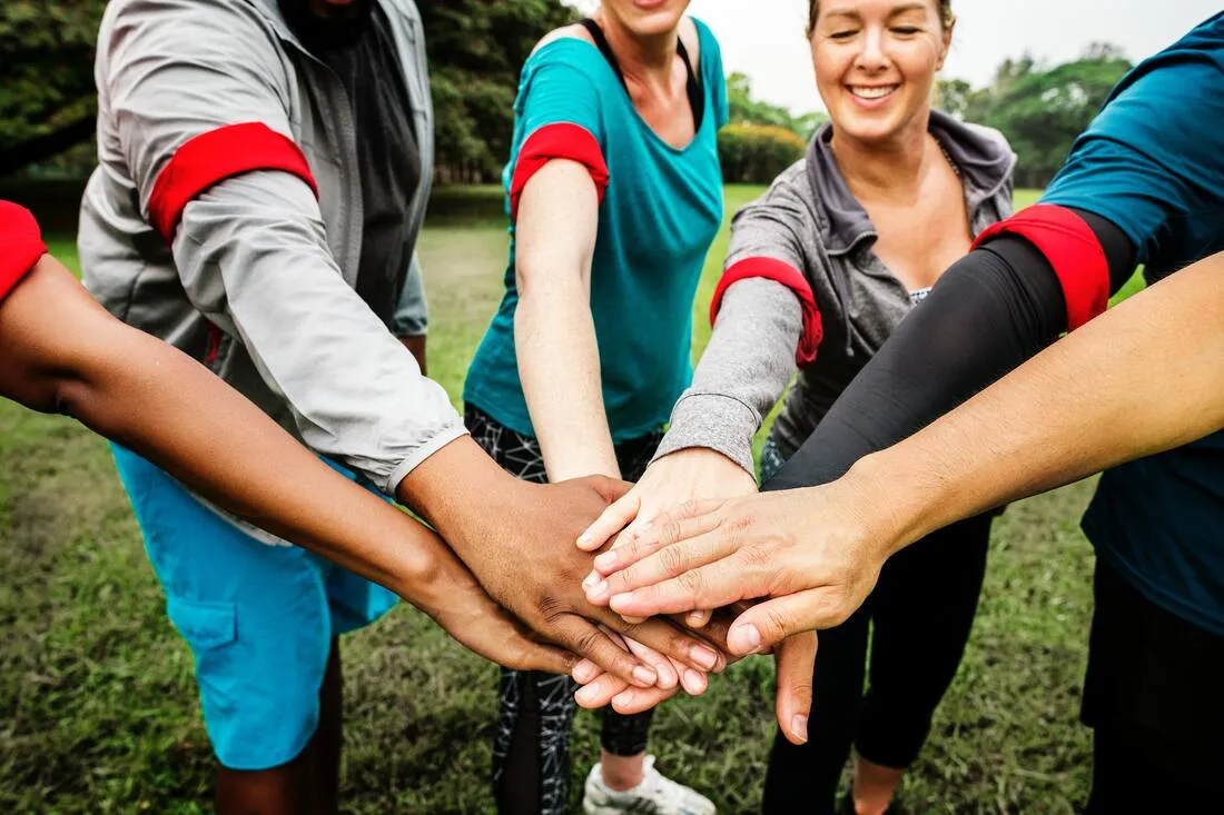 A group of people stacking their hands together in a team huddle outdoors