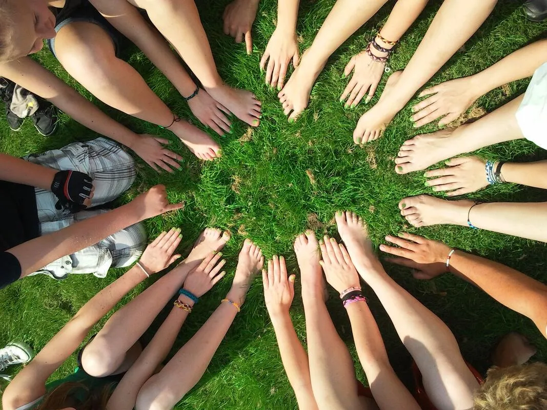 A circle of people with hands and feet together on the grass